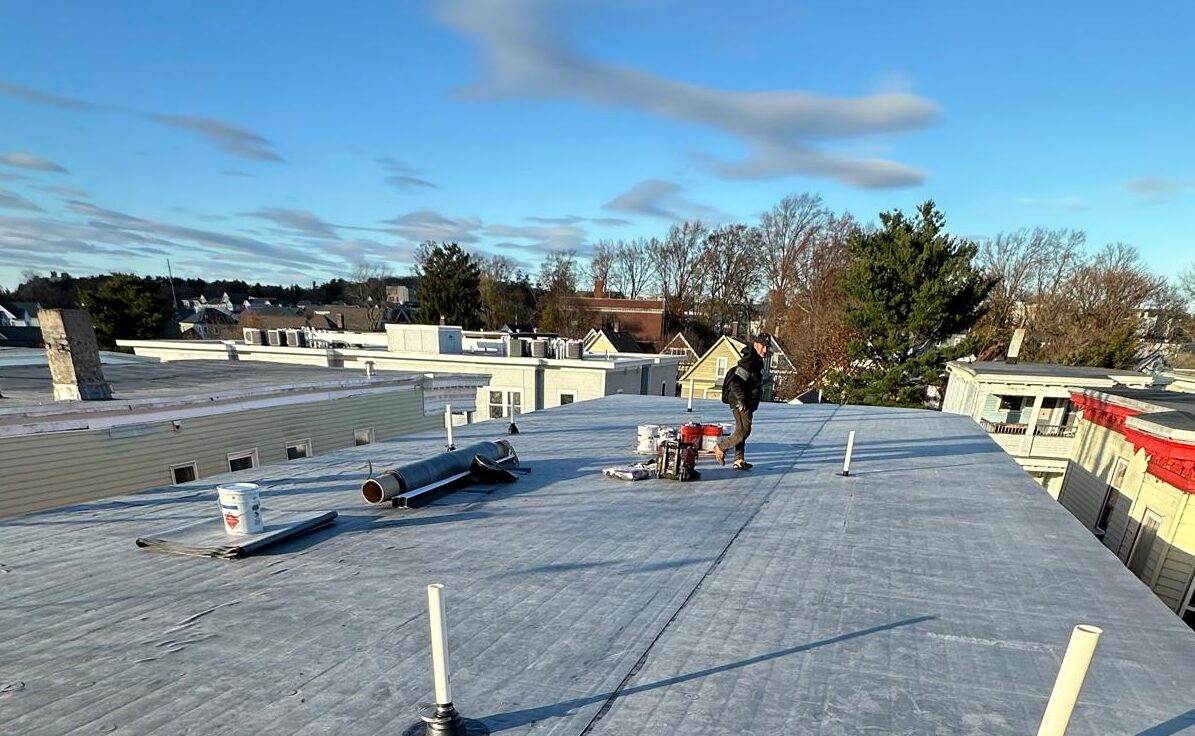 Flat roof with new rubber membrane and pipe boots, roofer in the distance (crop)
