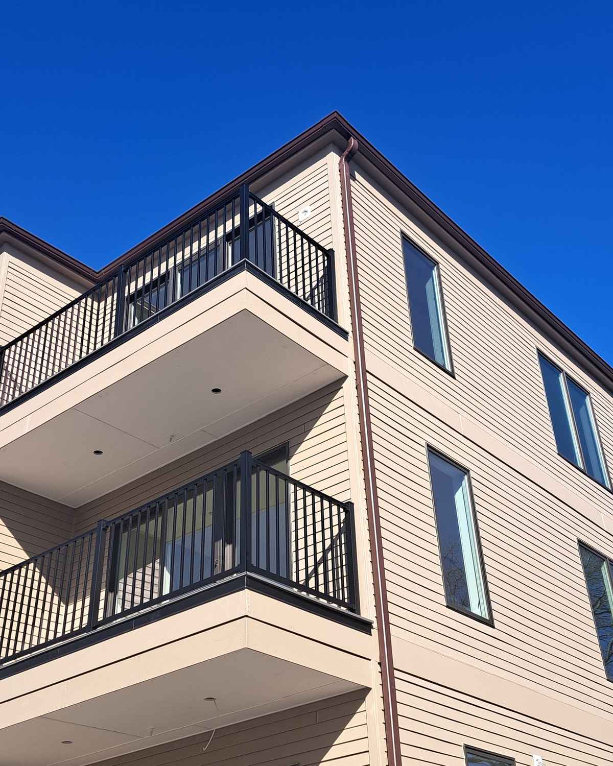 Looking up at a building corner with a dark box gutter, downspout and balconies