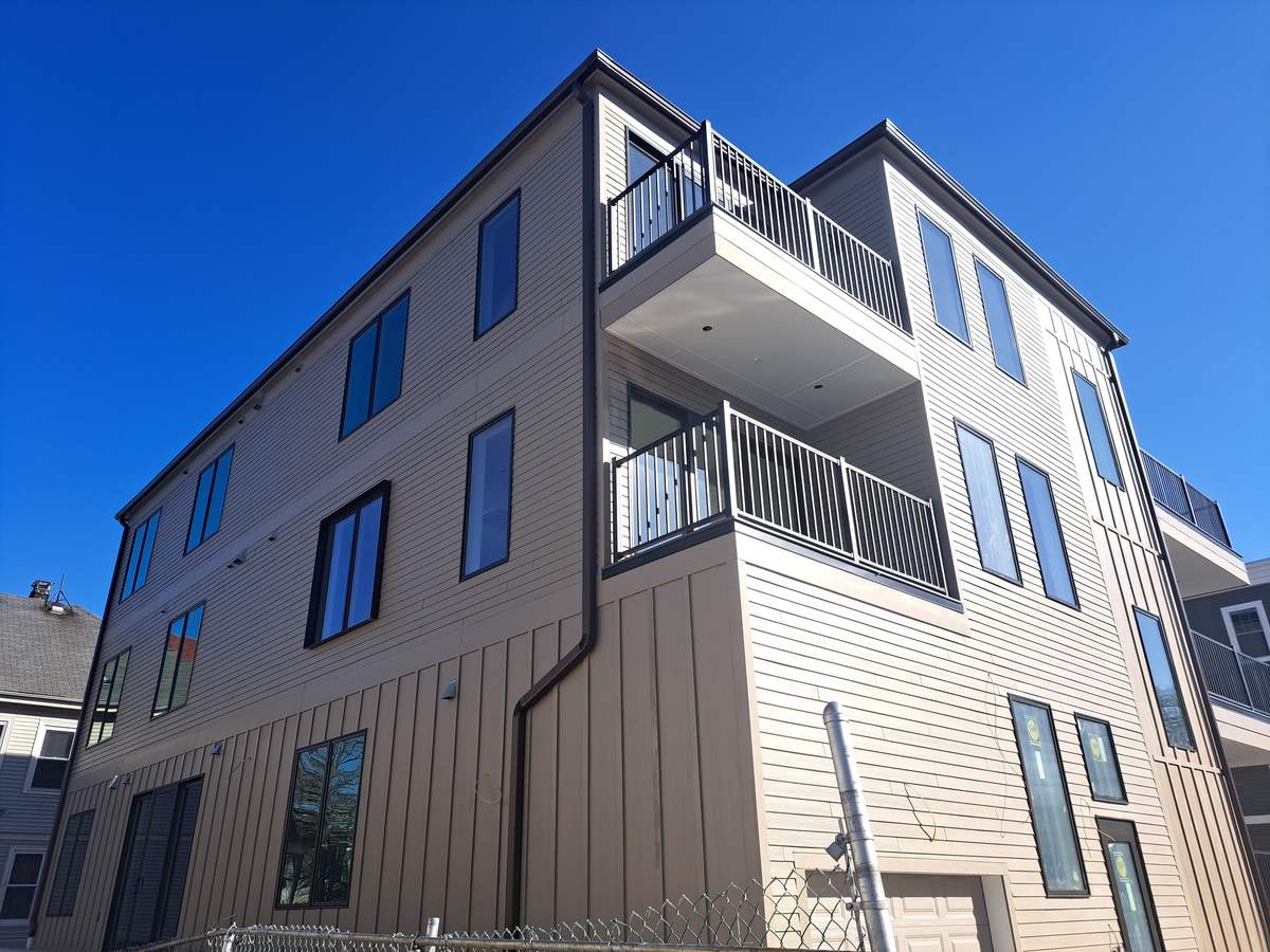 New three-story building with beige siding, dark seamless gutters, downspouts and balconies
