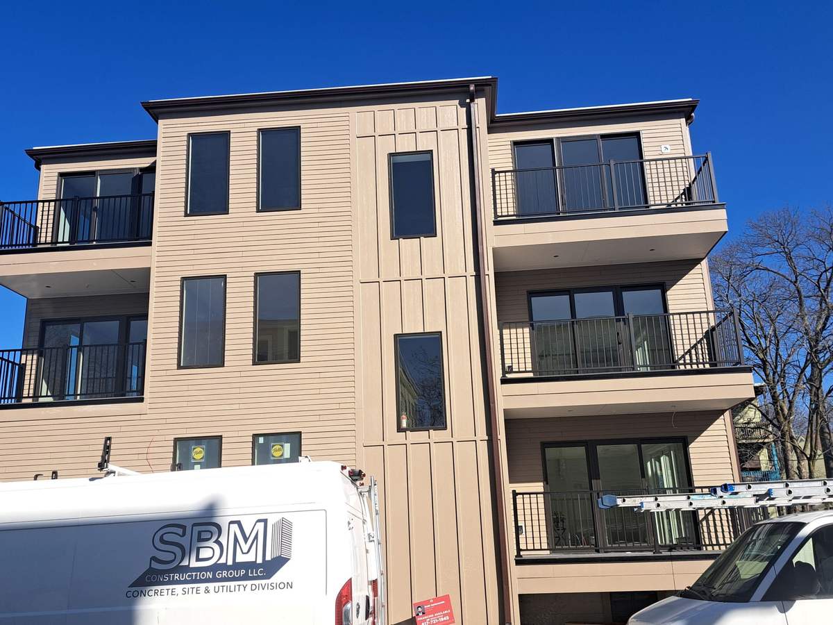 Front of a new three-story building with dark gutters and balconies, construction truck parked