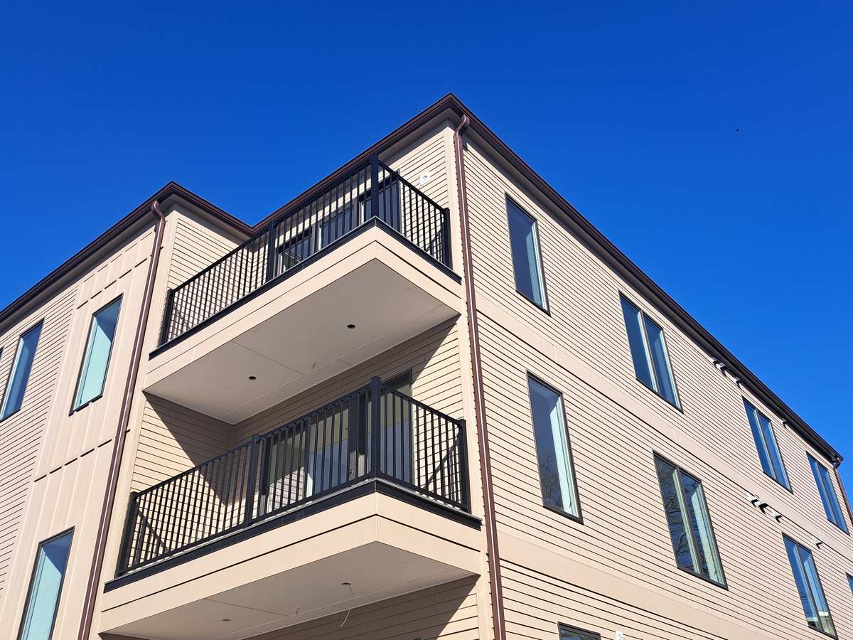 Looking up at a building corner with a dark box gutter, downspout and balconies