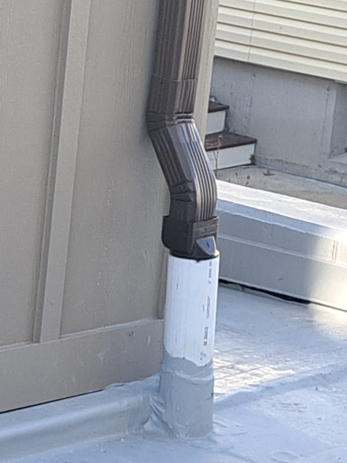 Downspout elbow connected to an underground drain at the base of a wall