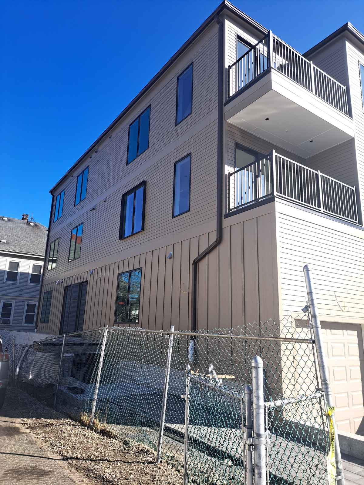 Corner of a new three-story building with a dark downspout and balconies