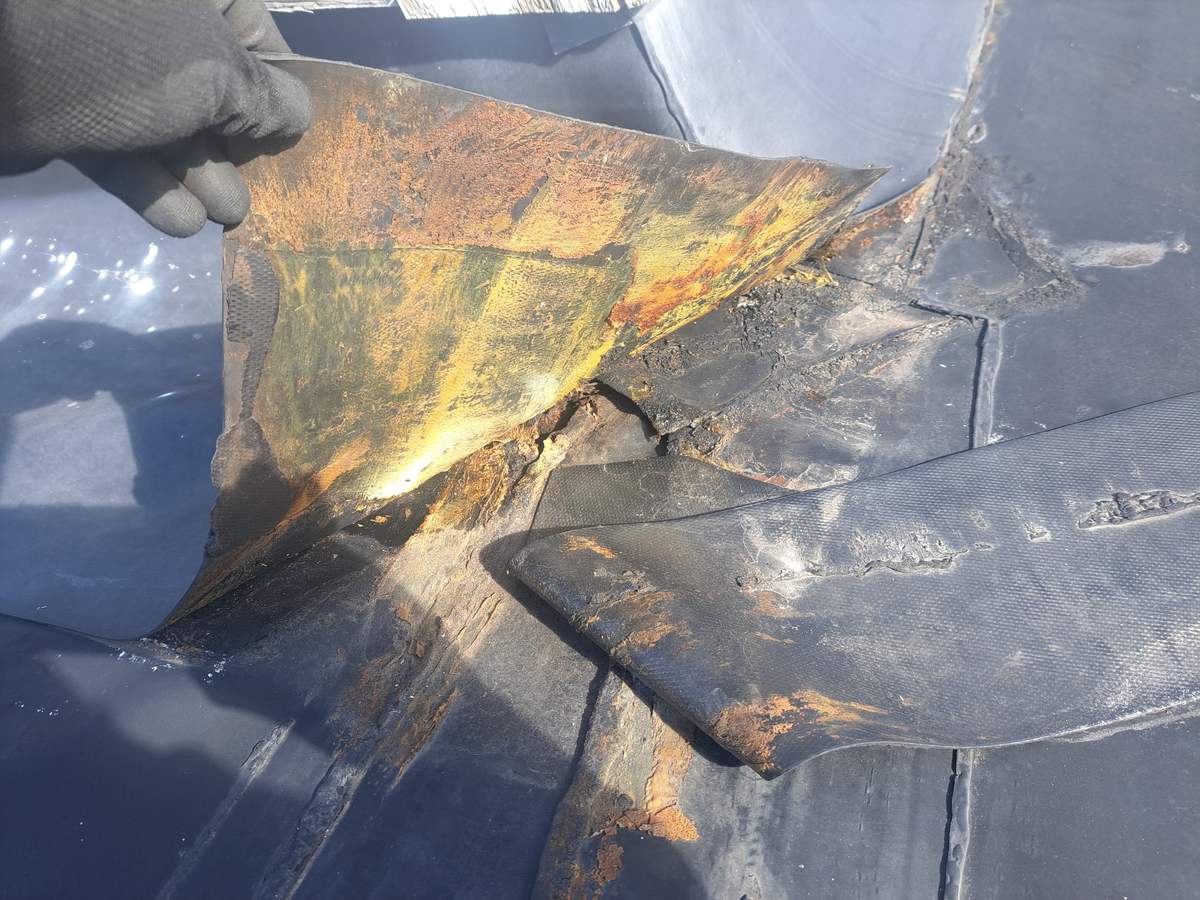 Gloved hand lifting rusted, rotted flashing on a rubber roof