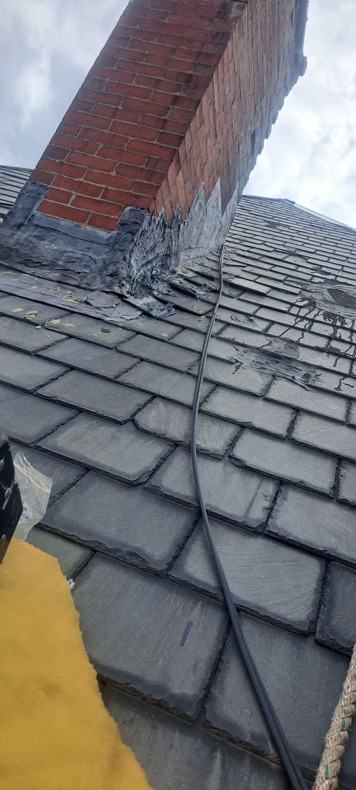 Slate roof repair beside a brick chimney