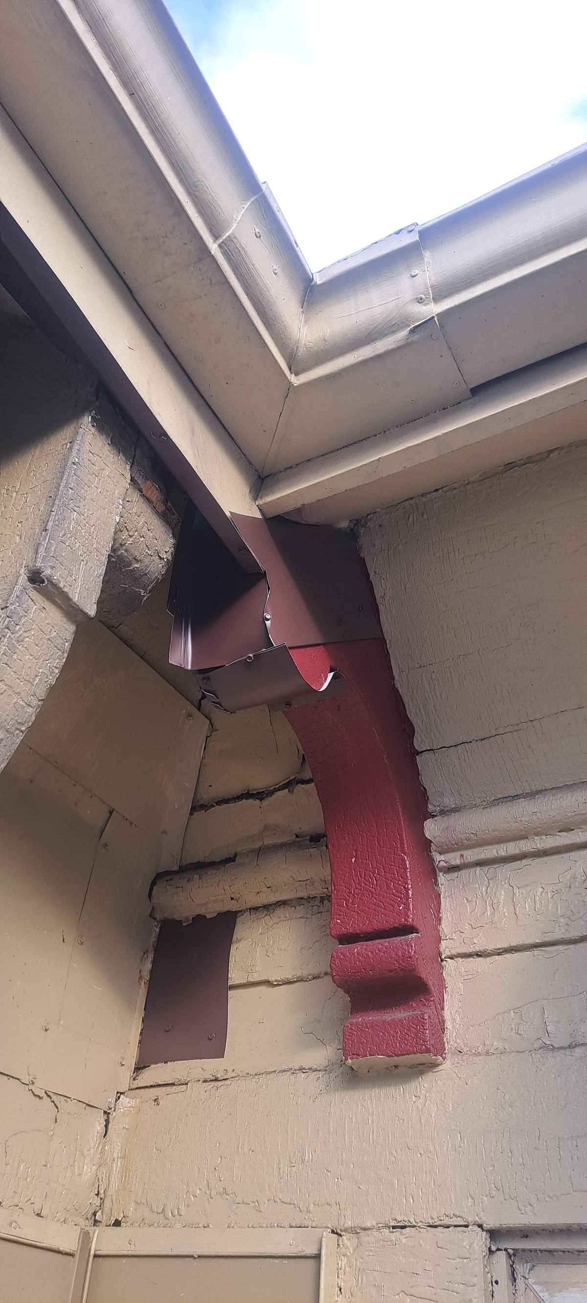 Roof eave corner with a red-painted bracket, gutter and repaired soffit
