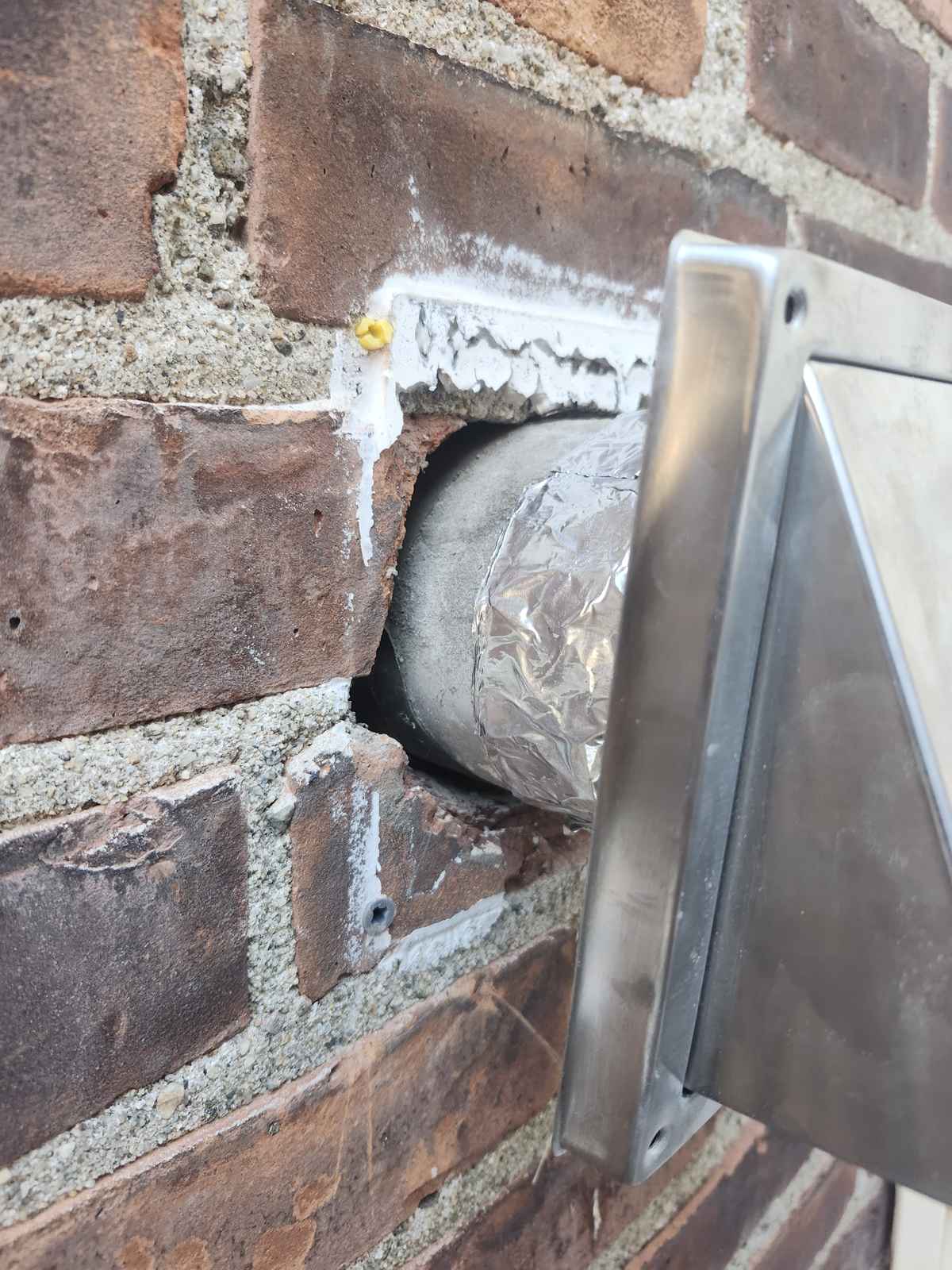 Stainless vent cap being installed through a brick wall with sealant