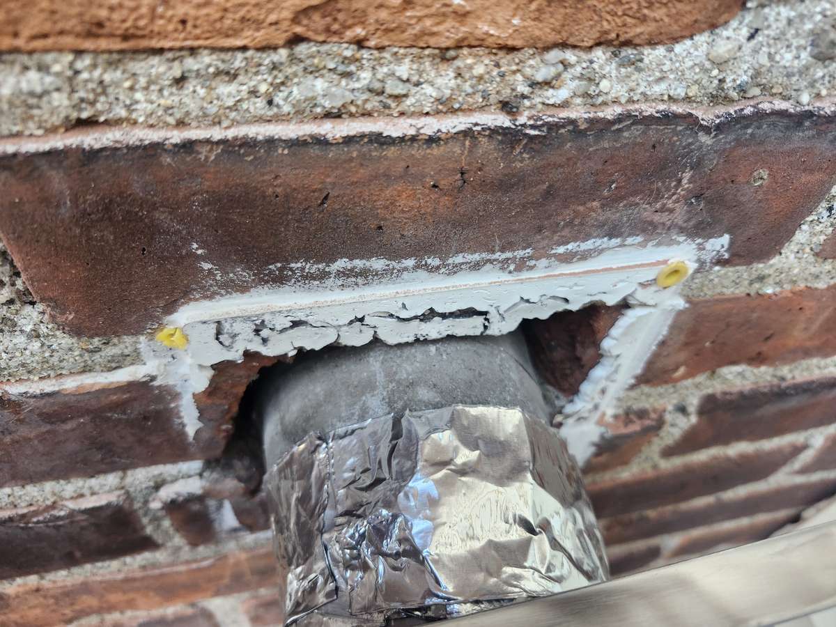 Opening cut in a brick wall with a foil-wrapped duct before installing a vent