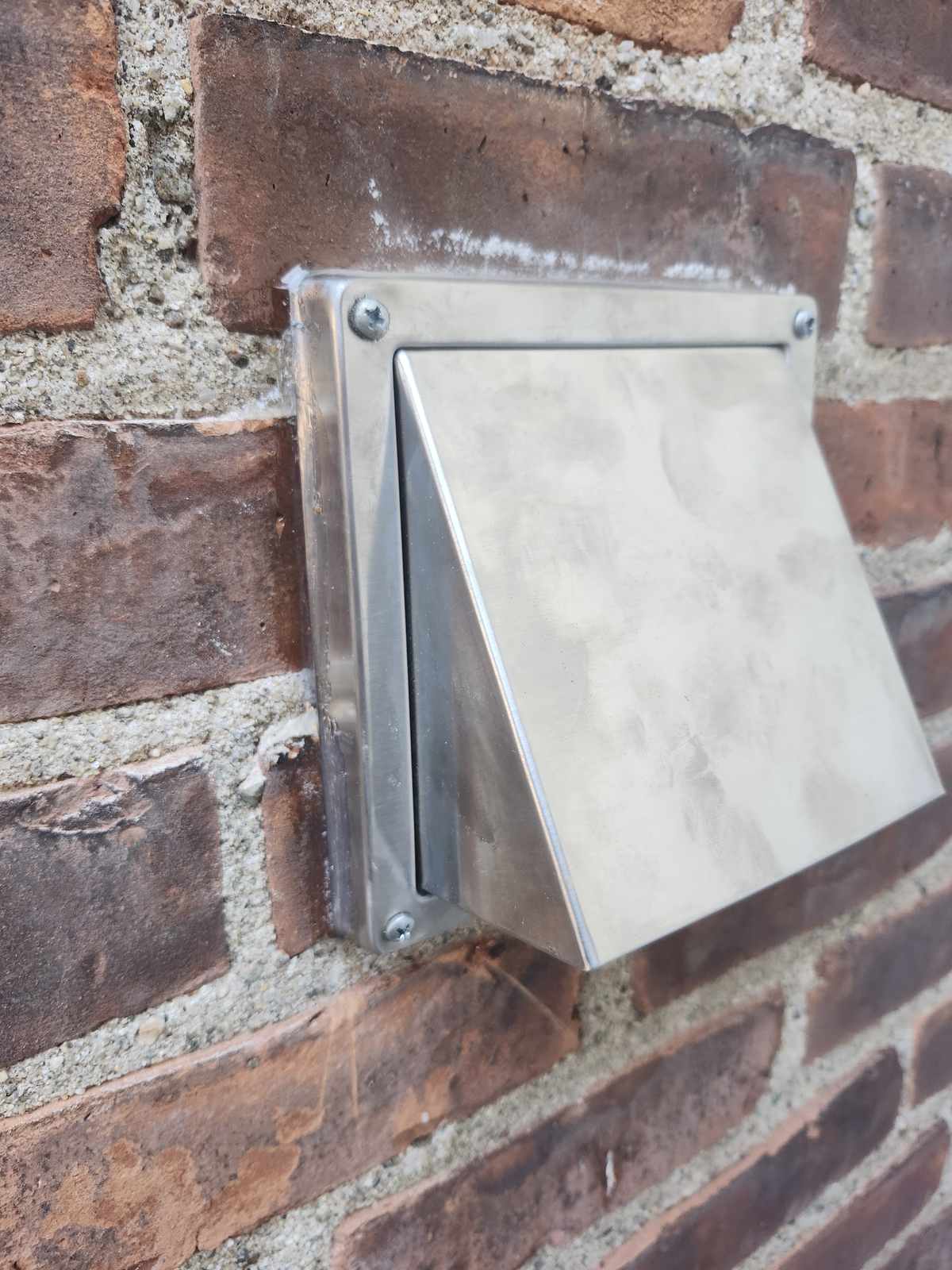 New stainless steel vent cap installed on a brick wall