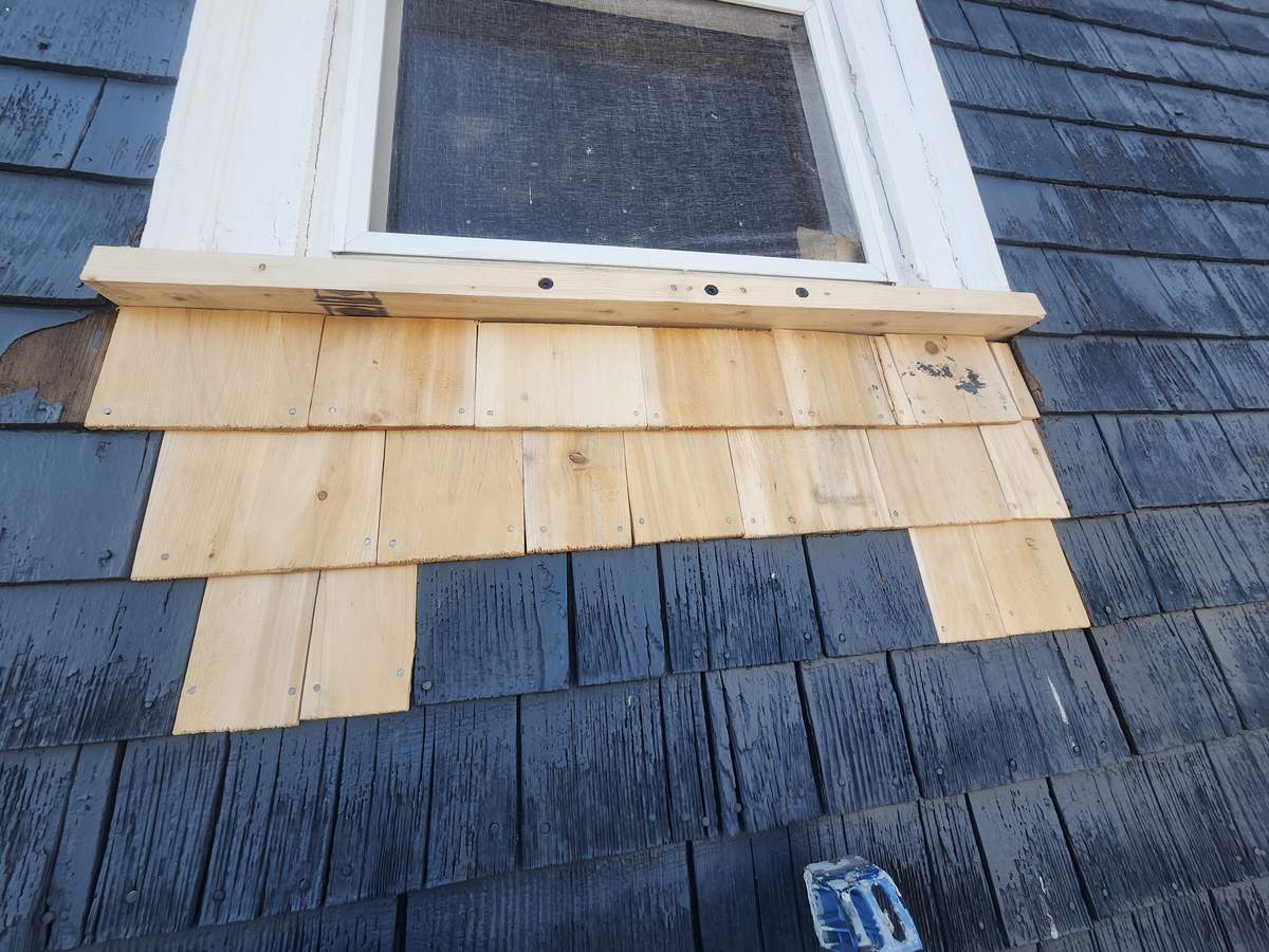 New cedar shingles replacing rotted siding below a window on a blue house