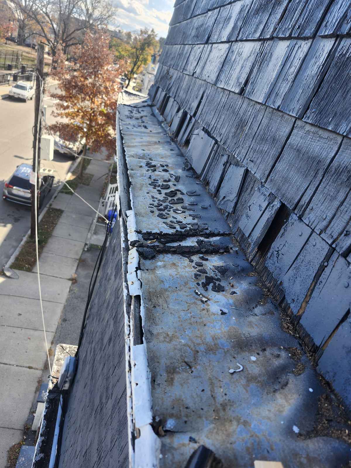 Slate roof edge and gutter with debris before cleaning and repair, street below