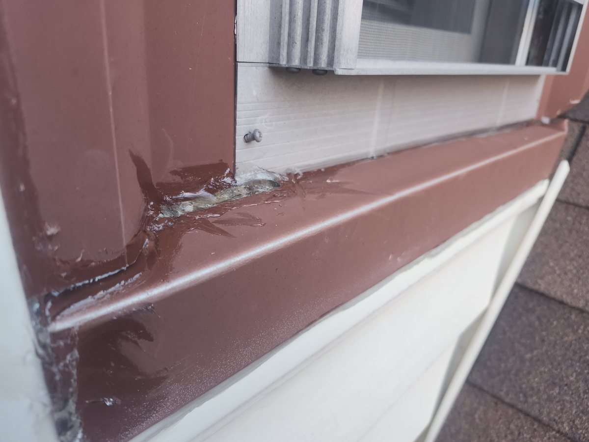 Brown aluminum trim being sealed where a window meets the siding