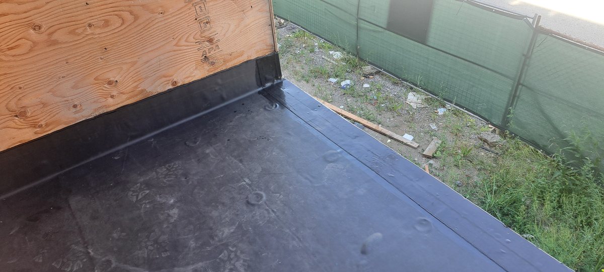 Black EPDM rubber membrane at a flat roof corner with drip edge and wood parapet