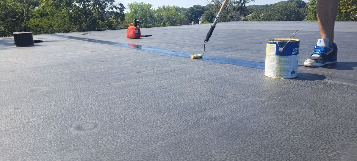 Roofer rolling adhesive on a large flat rubber roof
