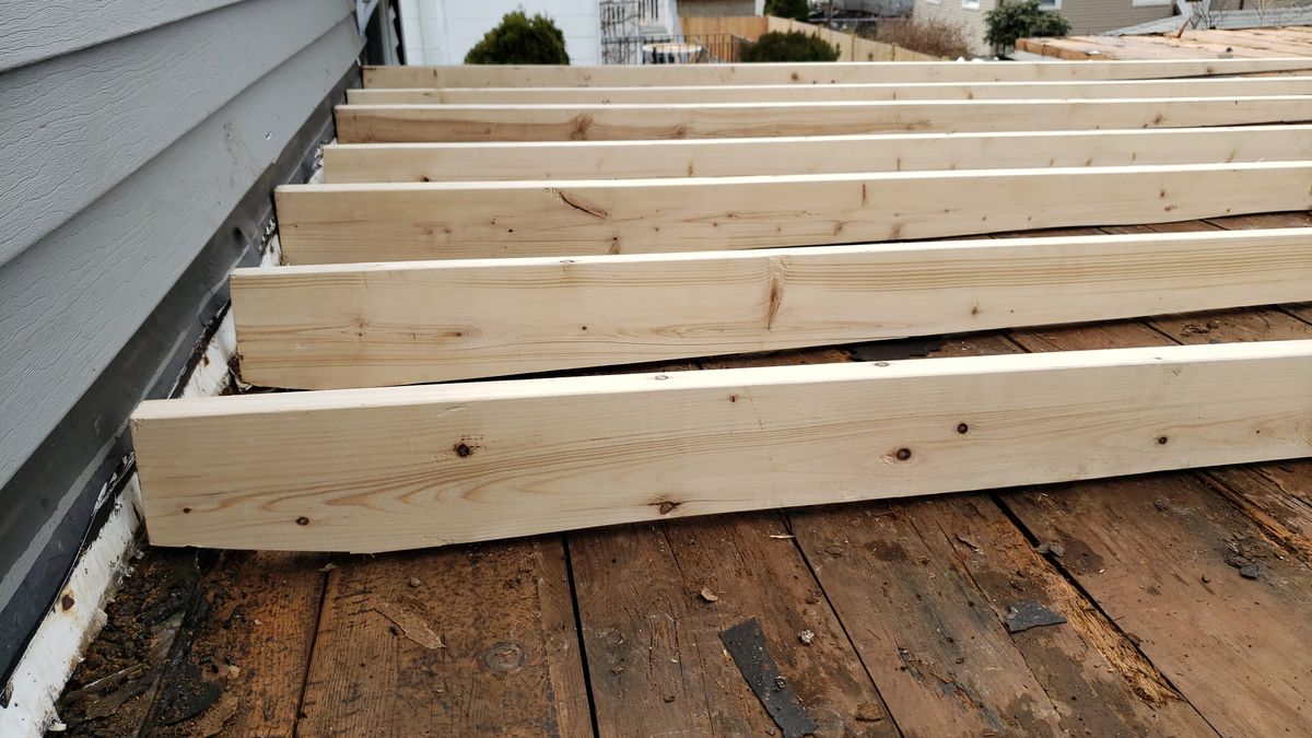 Close-up of new joists on an old wood roof deck beside siding