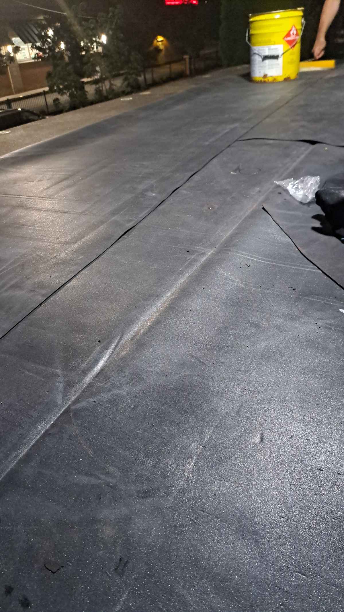 Rubber membrane seam being installed on a flat roof with an adhesive bucket