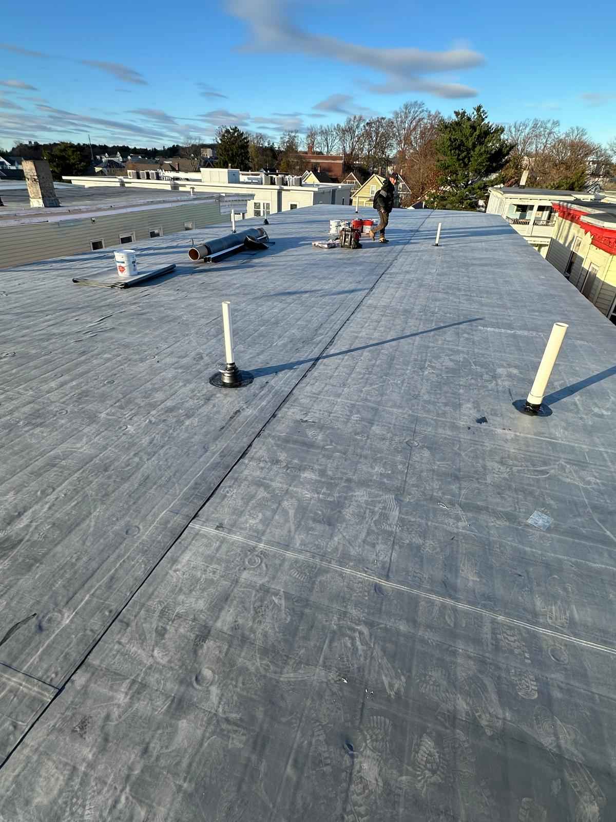 Flat roof with new rubber membrane and pipe boots, roofer working in the distance