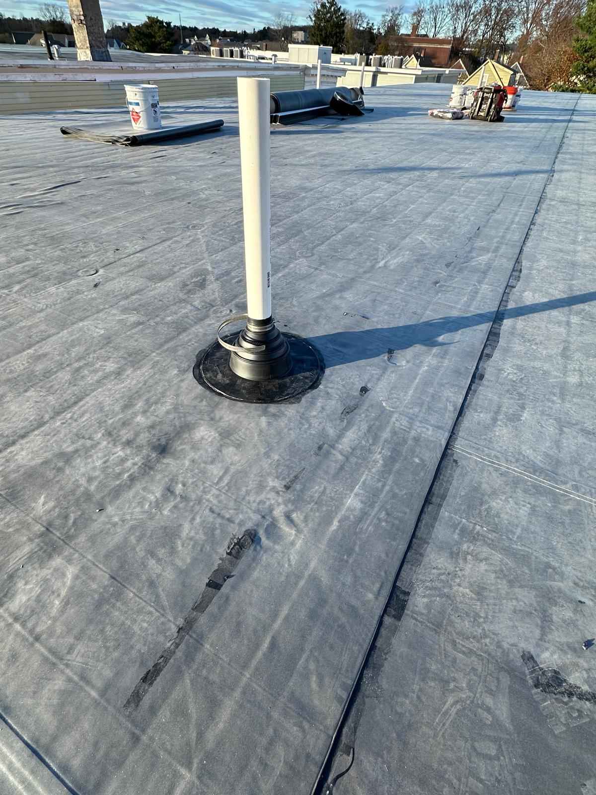 Flat rubber roof with a pipe boot and a roofer in the distance