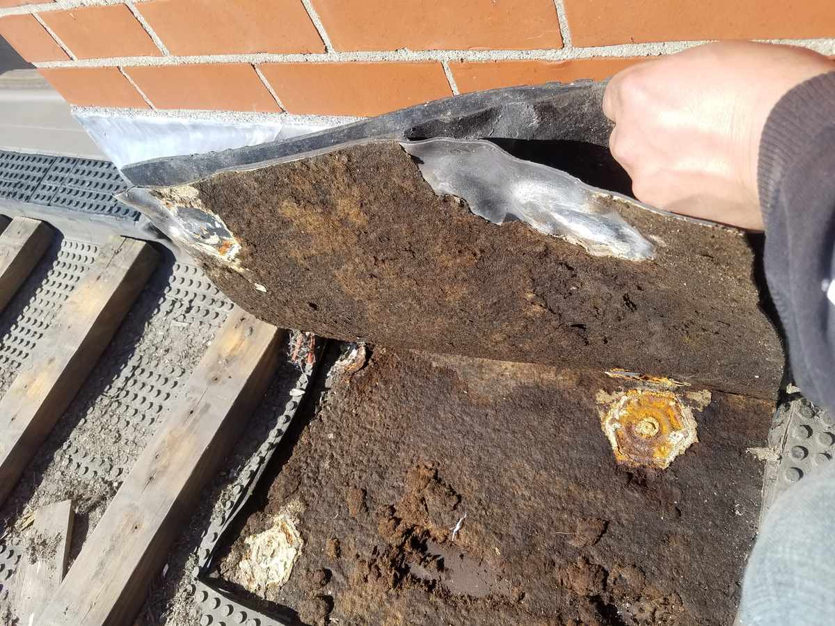 Hand lifting rusted, rotted roof edge flashing at a brick wall