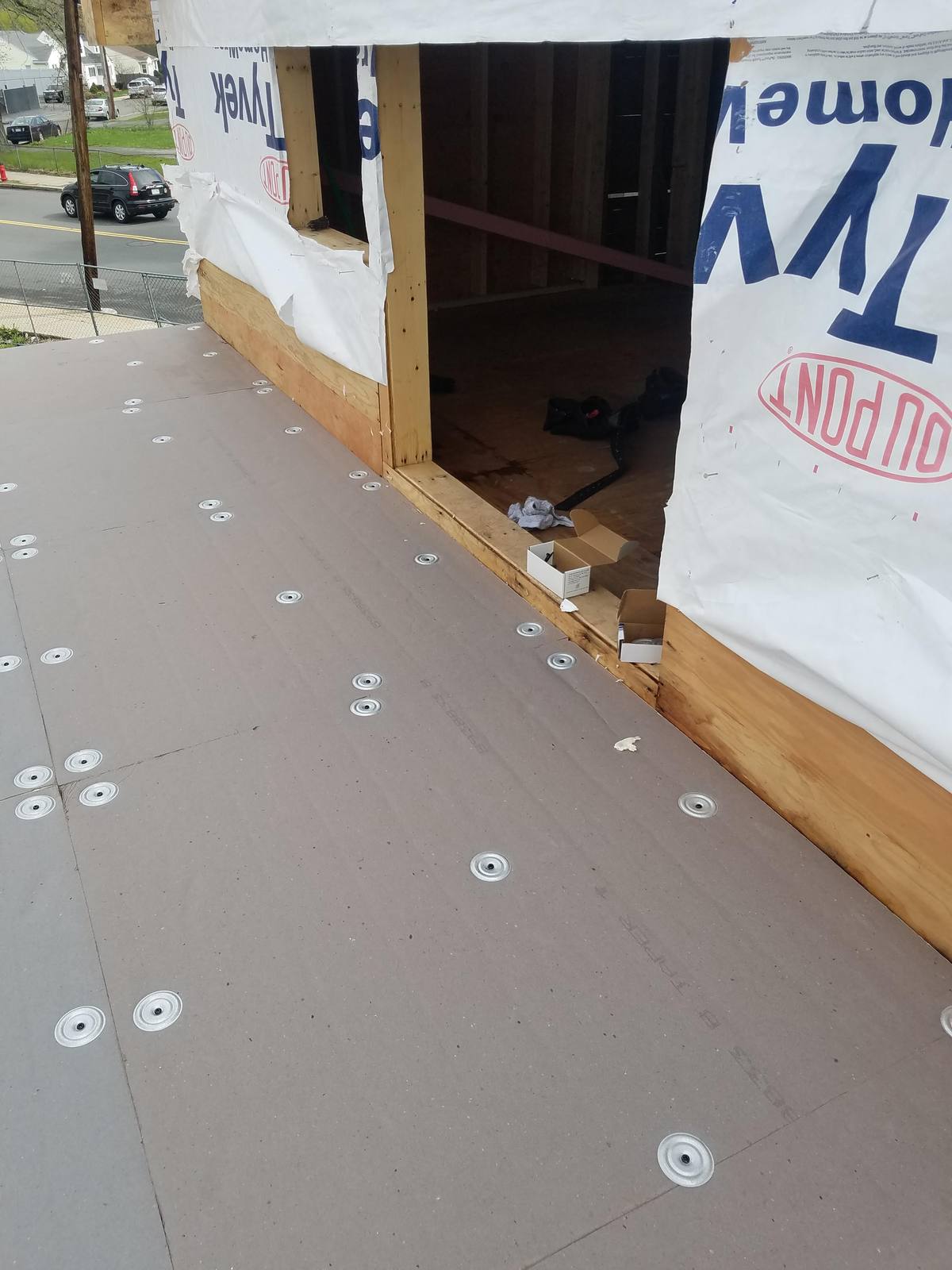 Insulation boards fastened with plates on a flat roof beside a wall with house wrap