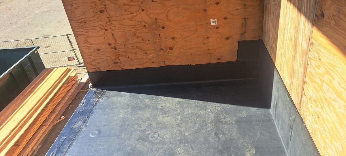 Black rubber membrane running up a plywood parapet at a flat roof corner