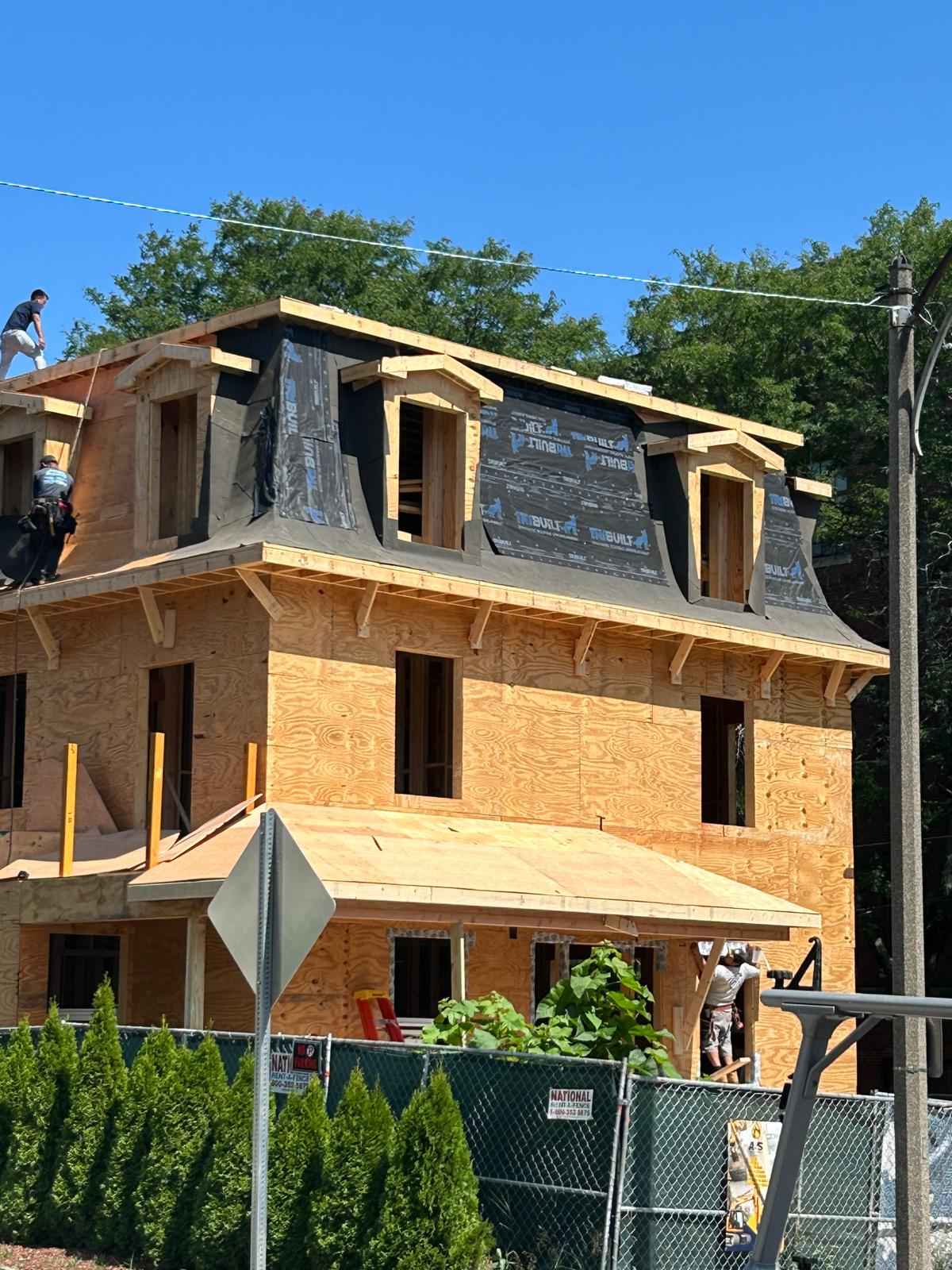Newly framed house with a mansard roof and dormers, roofers installing shingles on top