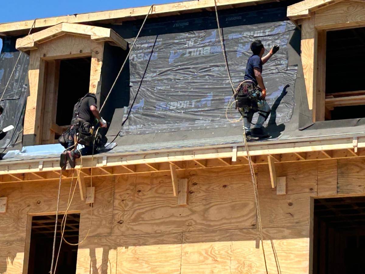 Two roofers in harnesses working on a dormer of a newly framed house