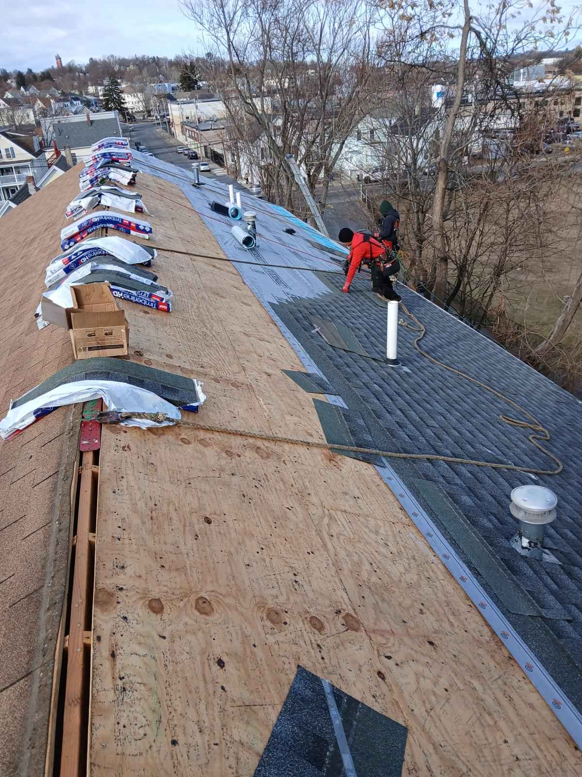 Roof deck being covered with synthetic underlayment, roofer and shingle bundles at the ridge