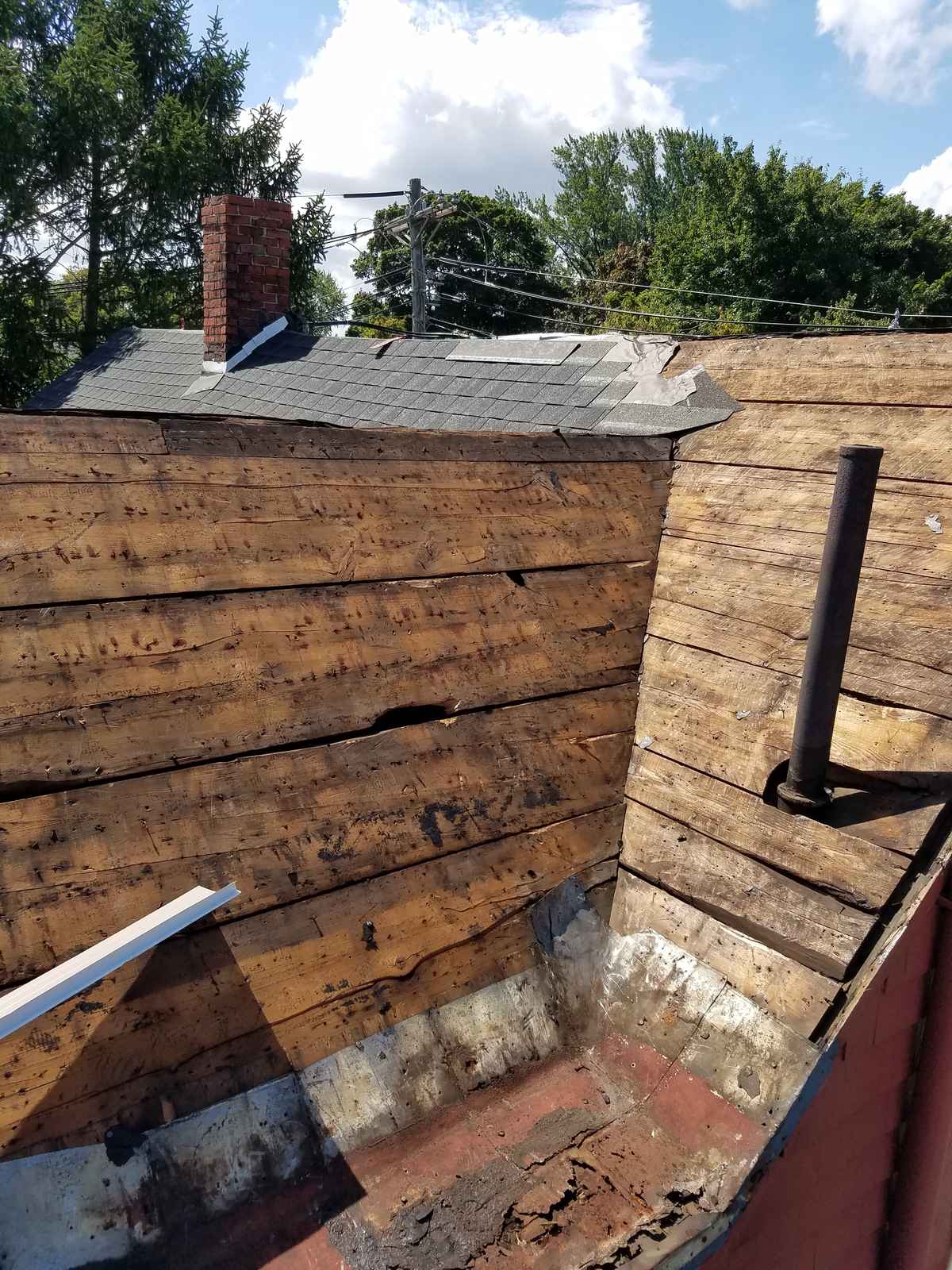 Stripped roof showing old board sheathing and a chimney before new shingles