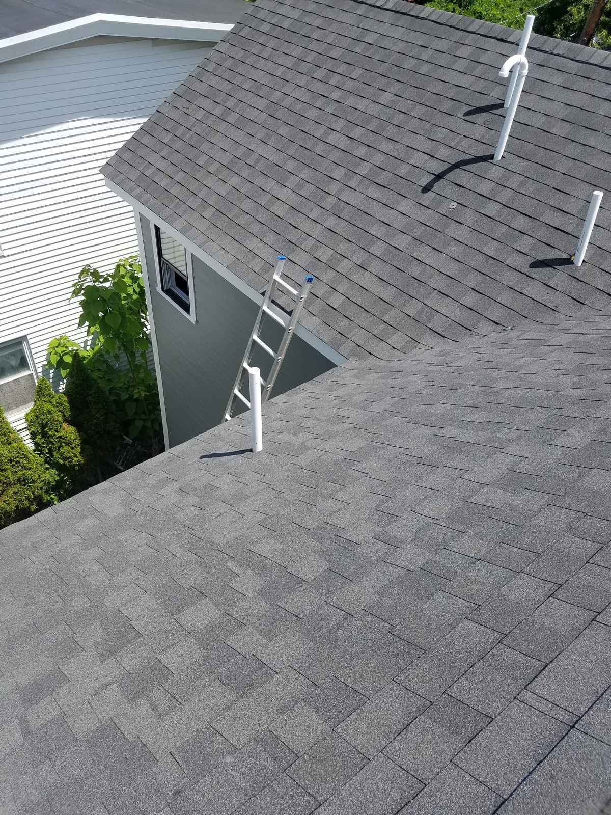 New gray shingle roof with ridge vent and pipe boots next to a white house