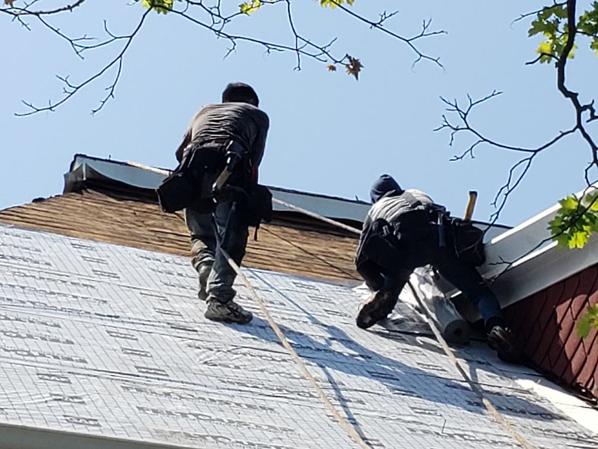 Two roofers in harnesses installing synthetic underlayment on a steep roof