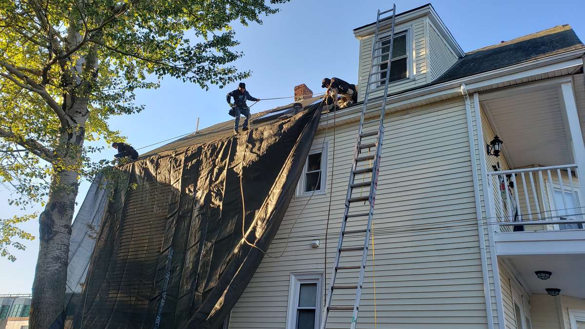 Roofers stripping old shingles from the steep roof of a yellow house