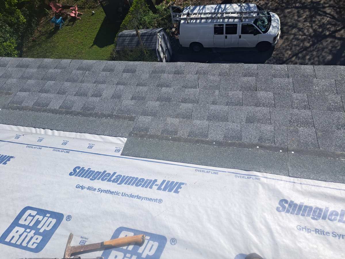 Synthetic underlayment and new shingles on a roof, work van parked in the yard below