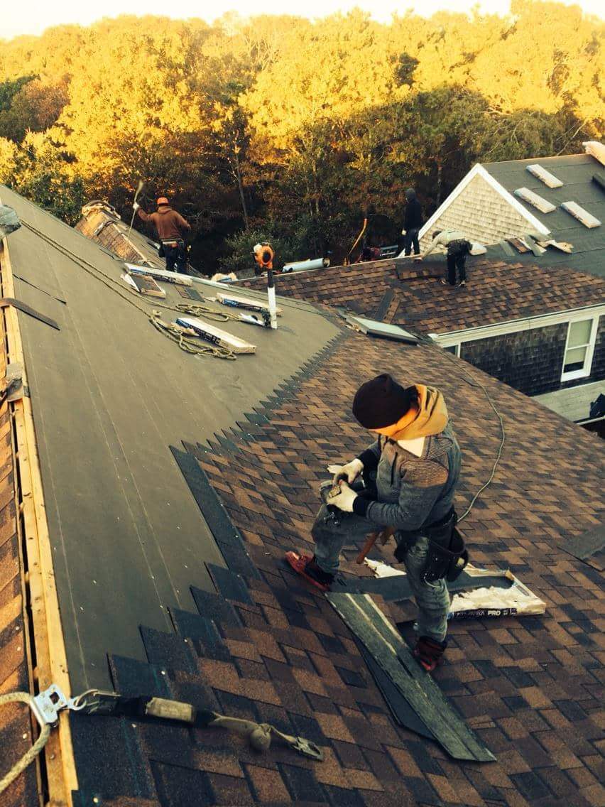 Roofer installing brown architectural shingles at sunset