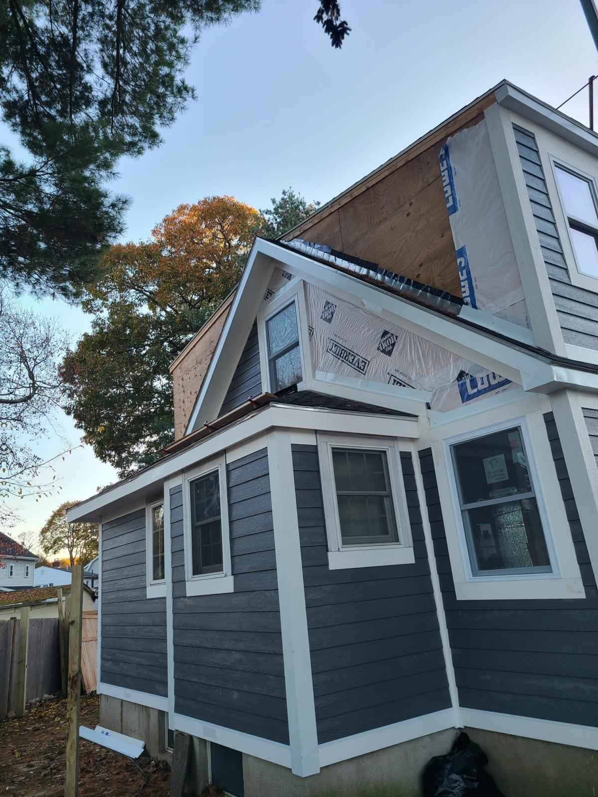 House with new dark gray siding and white trim, dormer addition under construction above