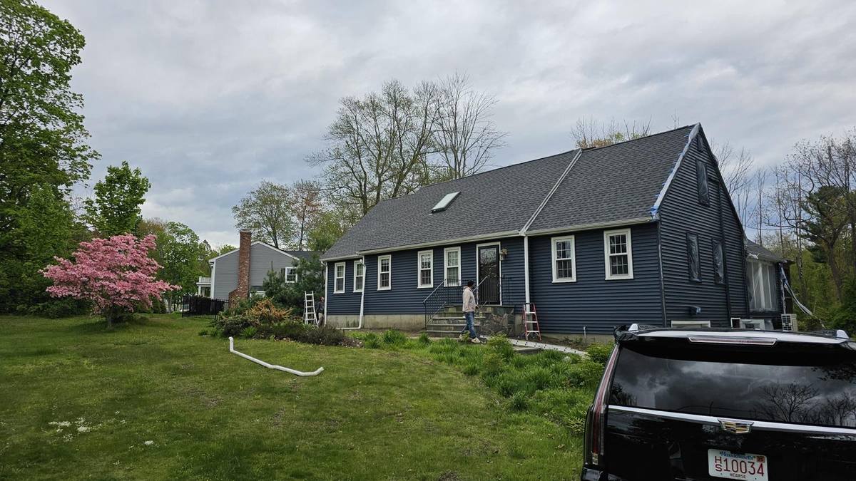 Cape-style house with a new gray shingle roof and dark siding in a spring garden