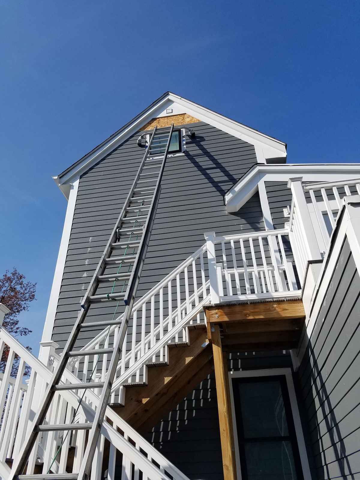 Rear of a house with new dark gray siding, white deck railings and a ladder