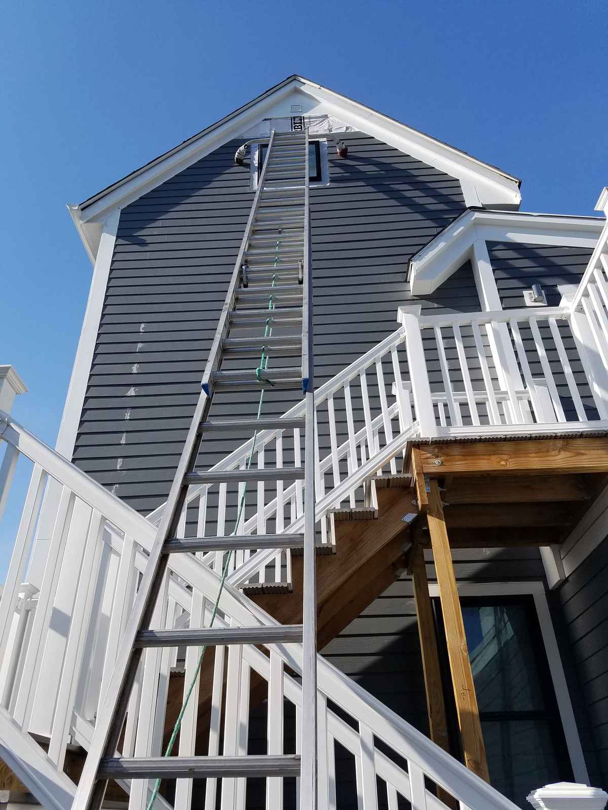 Rear of a multi-story house with new dark gray siding and white exterior stairs
