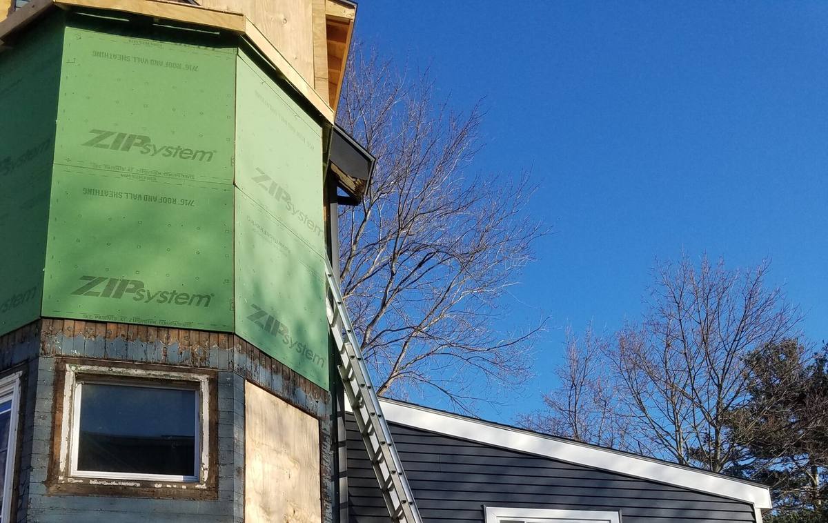 House corner sheathed with green ZIP System panels ready for siding, ladder in place