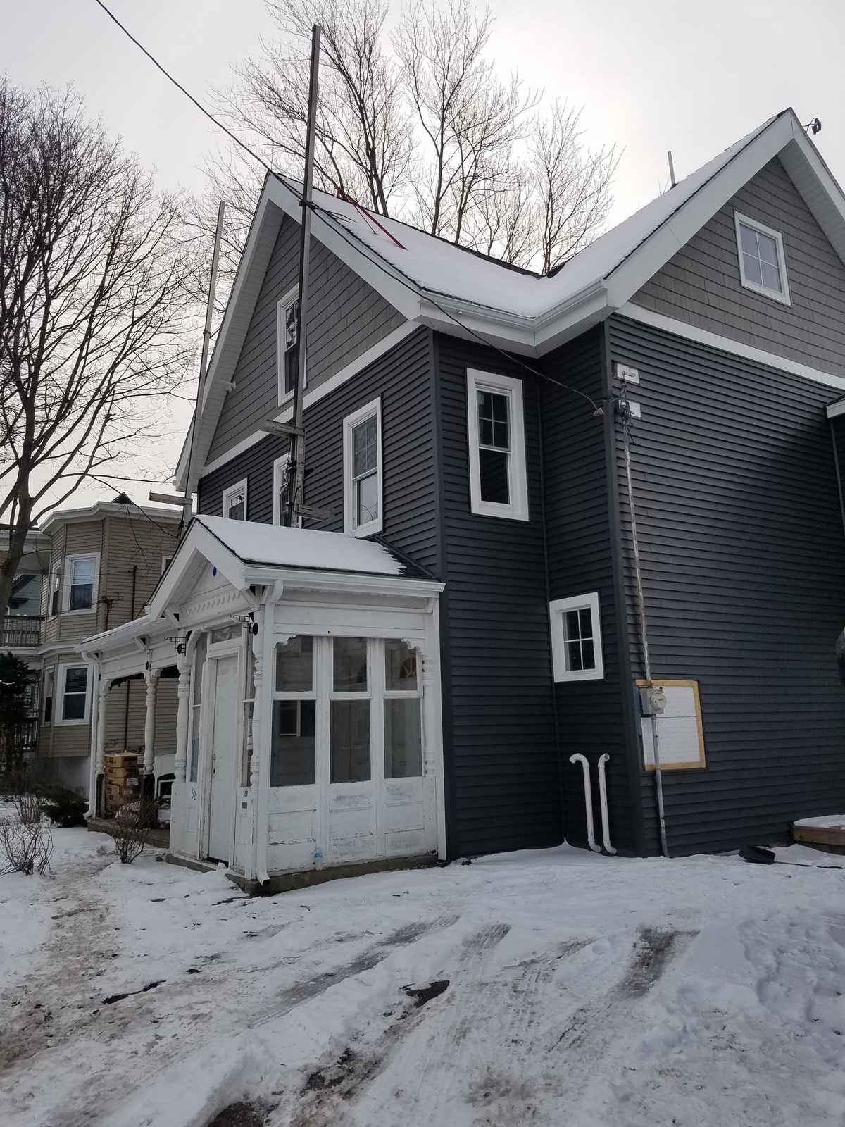 Two-story house with new dark gray siding, white trim and an enclosed porch, snow on the ground