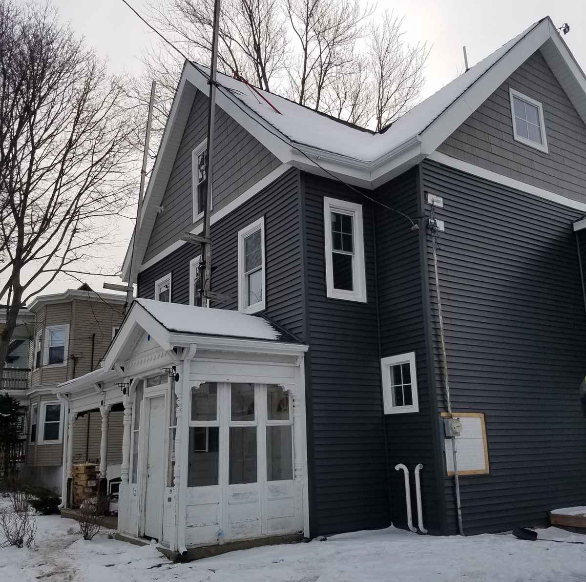 Two-story house with new dark gray siding, white trim and an enclosed porch in winter
